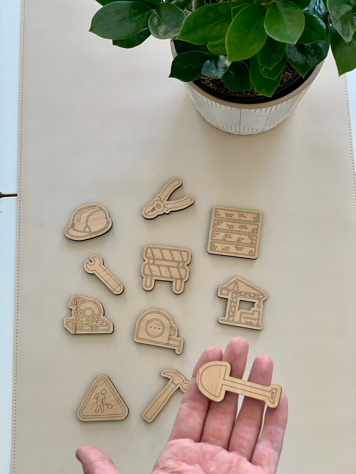 Set of eleven laser cut wooden construction and worksite themed loose parts on white surface with plant in background