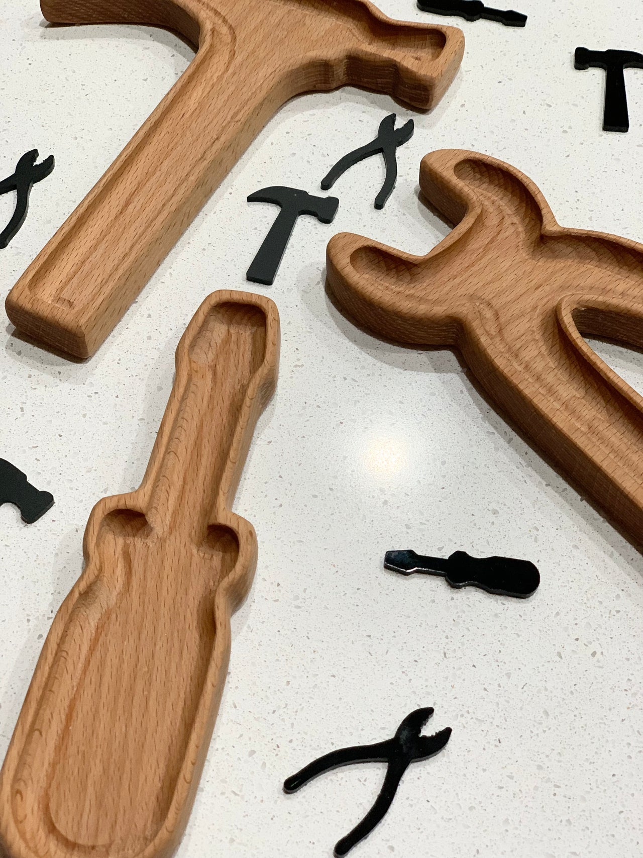 Wooden tool-shaped sensory trays with cutouts and small black tool-shaped pieces on white speckled surface