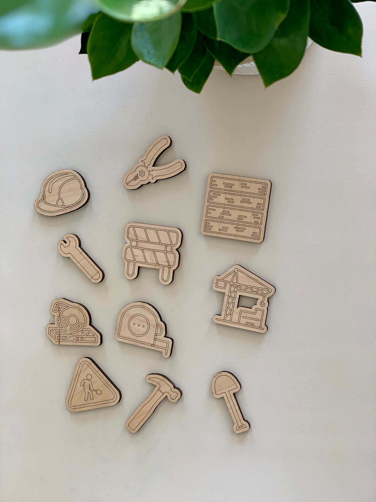 Set of 11 wooden construction and worksite themed loose parts including helmet, tools, caution sign, and building materials on white surface