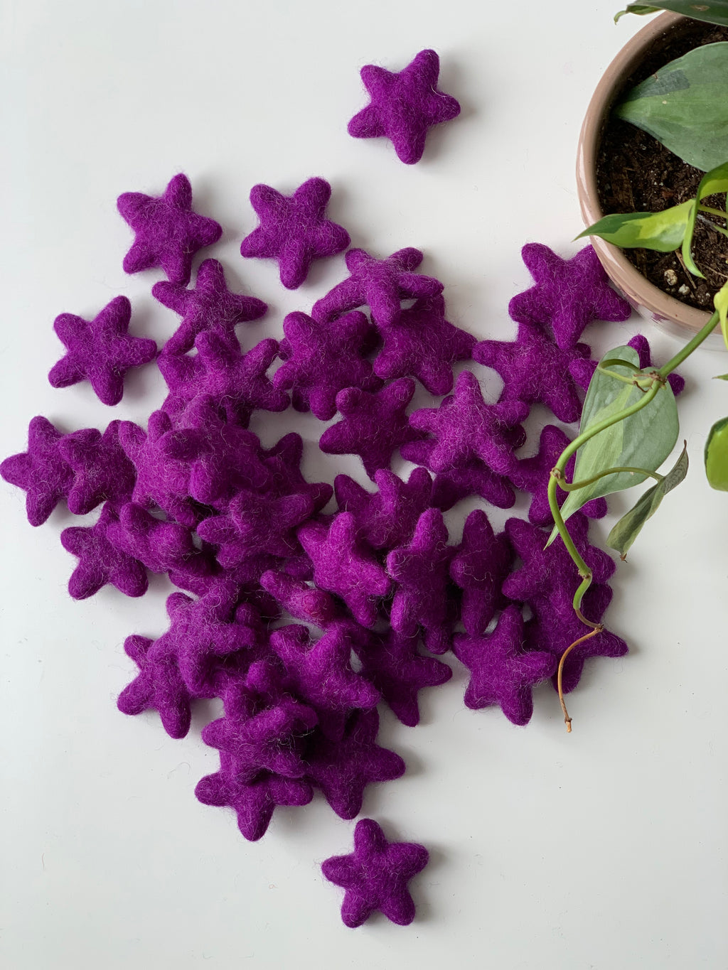 Pile of small handmade purple felt stars scattered near potted plant on white surface