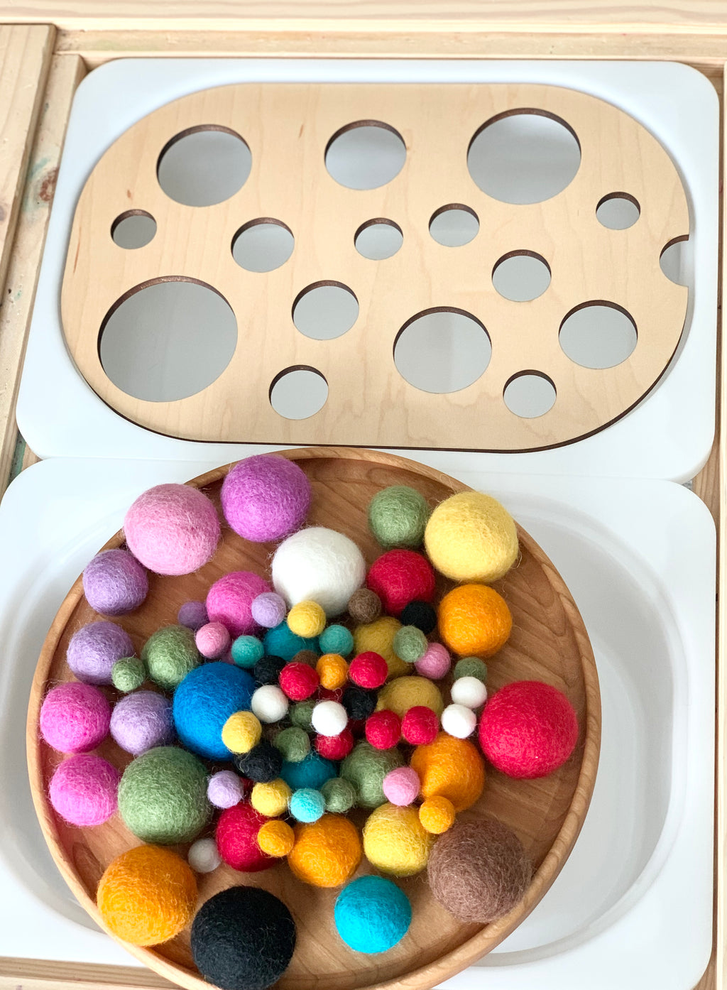 Wooden circle sorter Flisat table top insert with multicolored felt balls on wooden tray on white surface