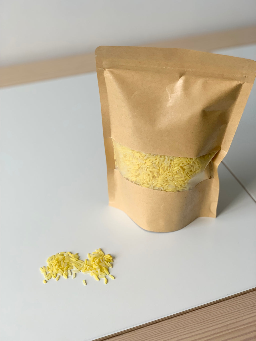Brown kraft paper pouch filled with yellow sensory rice filler with loose grains on white surface