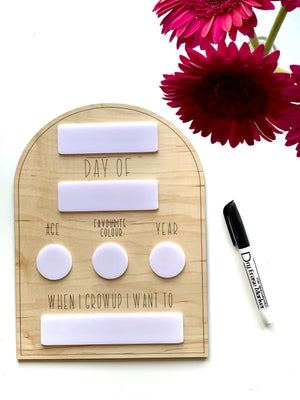 Natural wooden dry erase back to school sign with white writable sections and black marker next to pink flowers on white background