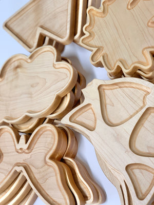 Stacked natural wooden sensory trays shaped like leaves, a bird, and a butterfly on white background