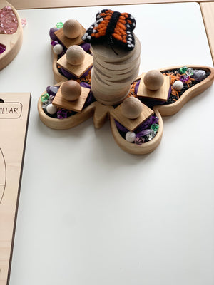 Butterfly-shaped wooden sensory tray with wooden blocks, beads, and colorful textured materials on white surface