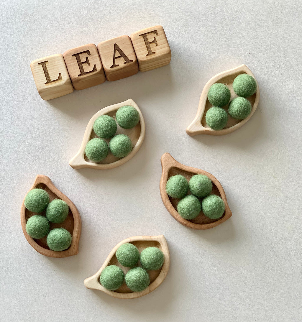 Small wooden leaf-shaped sensory trays filled with green felt balls and wooden letter blocks spelling LEAF on white surface