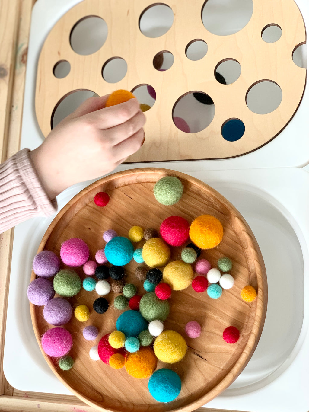 Child’s hand placing a felt ball into wooden Circle Ball Sorter Flisat table top insert with natural wood tray of colorful felt balls
