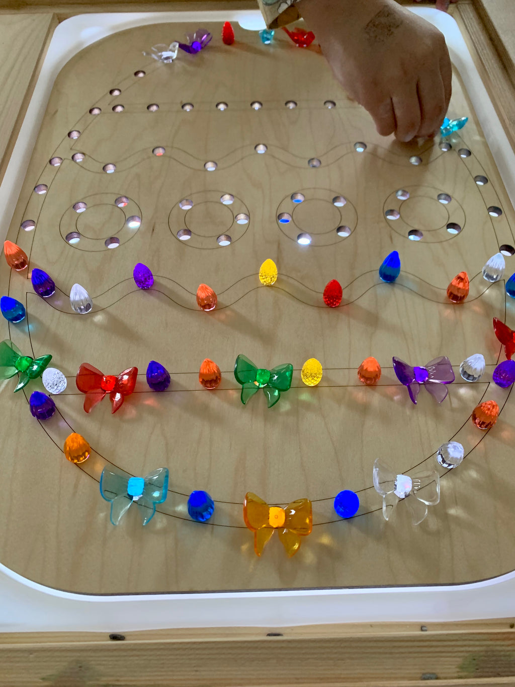Wooden Flisat tray shaped like an Easter egg with colorful light-up pegs inserted in holes on table surface
