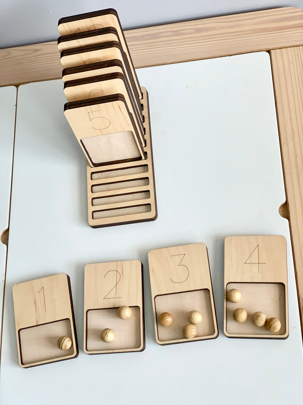 Wooden 1-10 counting trays with engraved numbers and matching wooden balls on white surface with vertical stand