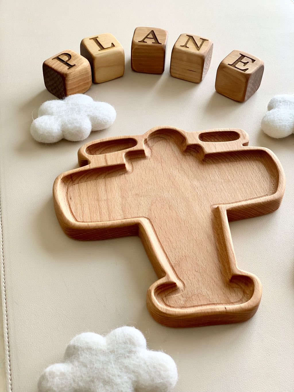 Wooden airplane-shaped sensory tray surrounded by felt clouds and wooden blocks spelling plane on white surface