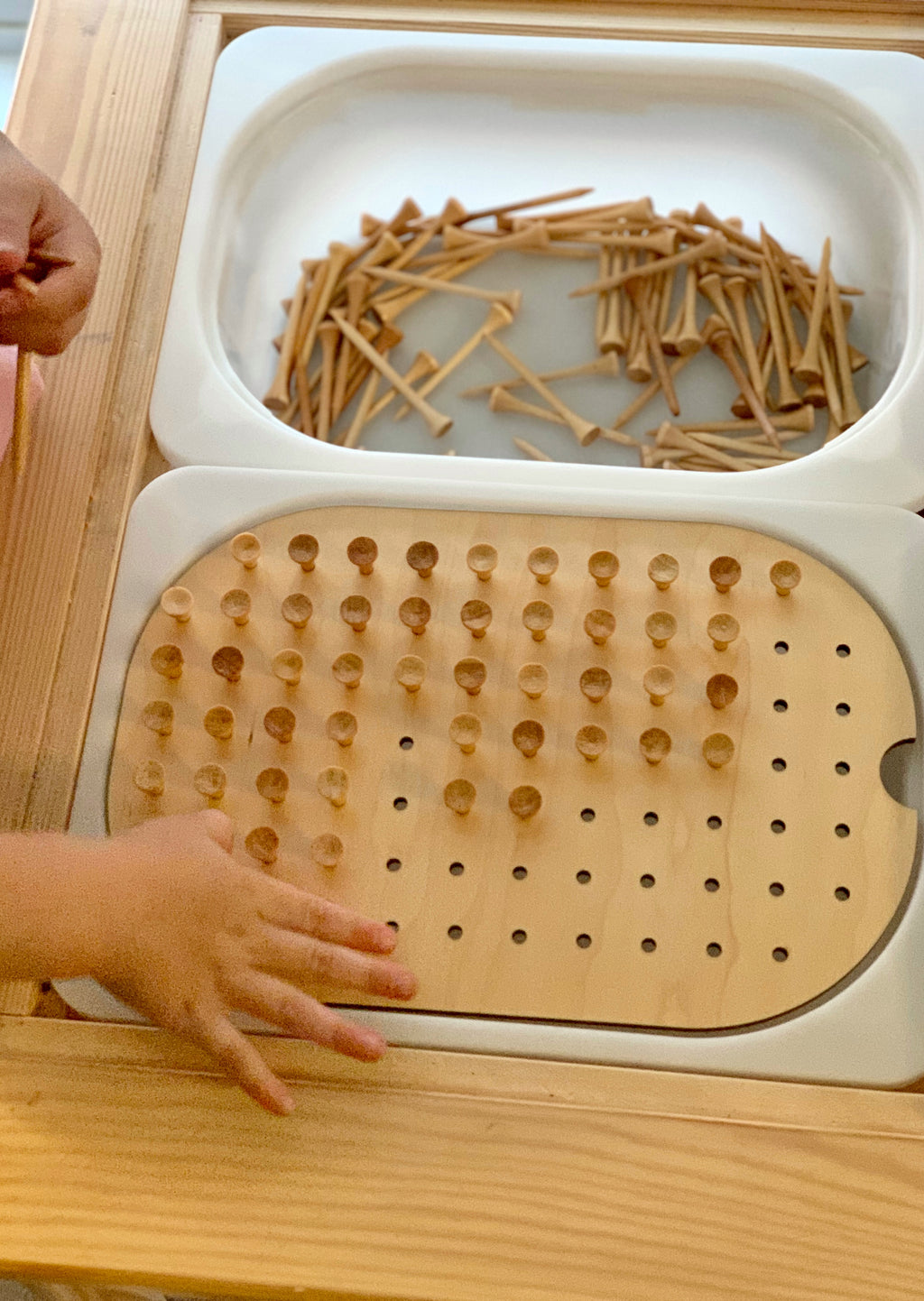 Wooden small hole peg board with geometric light board insert and scattered small wooden pegs on white tray