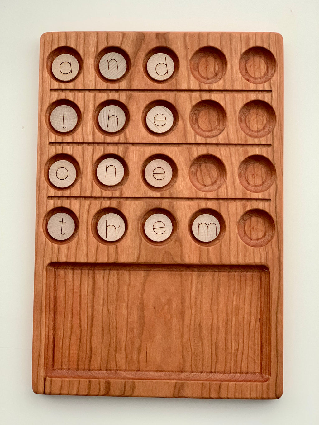 Natural wooden 20 frame sensory tray with engraved circles holding wooden alphabet discs spelling words on light wood background