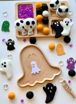 Natural wooden ghost-shaped sensory tray with colorful felt balls and spooky Halloween-themed felt decorations scattered on white surface