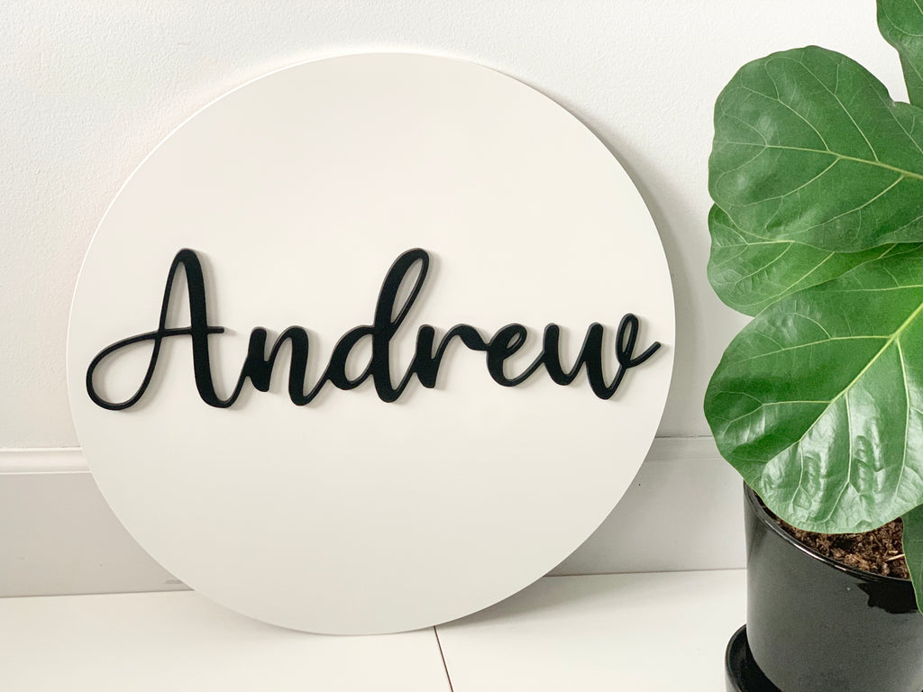 3D round name sign with black cursive letters on white background next to a green leafy plant in black pot