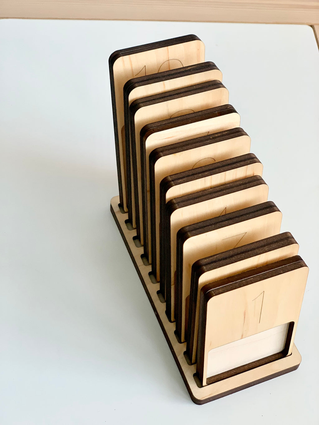Natural wooden 1-10 counting trays with engraved numbers arranged upright in a wooden stand on white surface