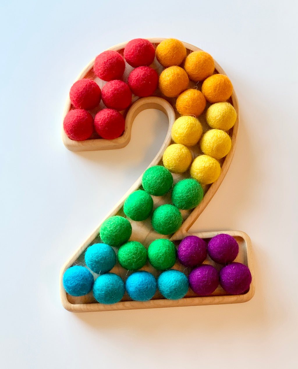 Natural wooden number tray shaped as 2 filled with colorful felt balls in rows on white background