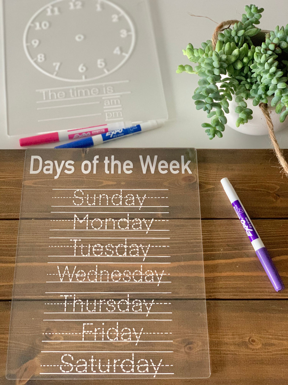 Clear acrylic Days of the Week tracing board with white dotted letters and purple dry erase marker on wooden table