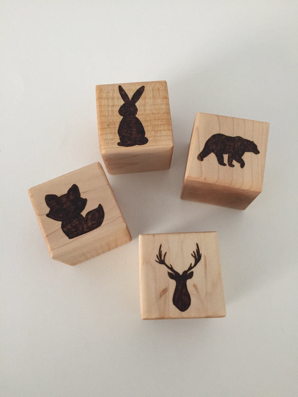 Natural wooden 1.5 inch blocks with engraved animal silhouettes including rabbit, bear, fox, and deer on light wood background