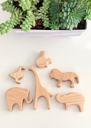 Natural wooden safari animal toy figurines including lion, giraffe, elephant, rhino, duck, and hippopotamus on white surface