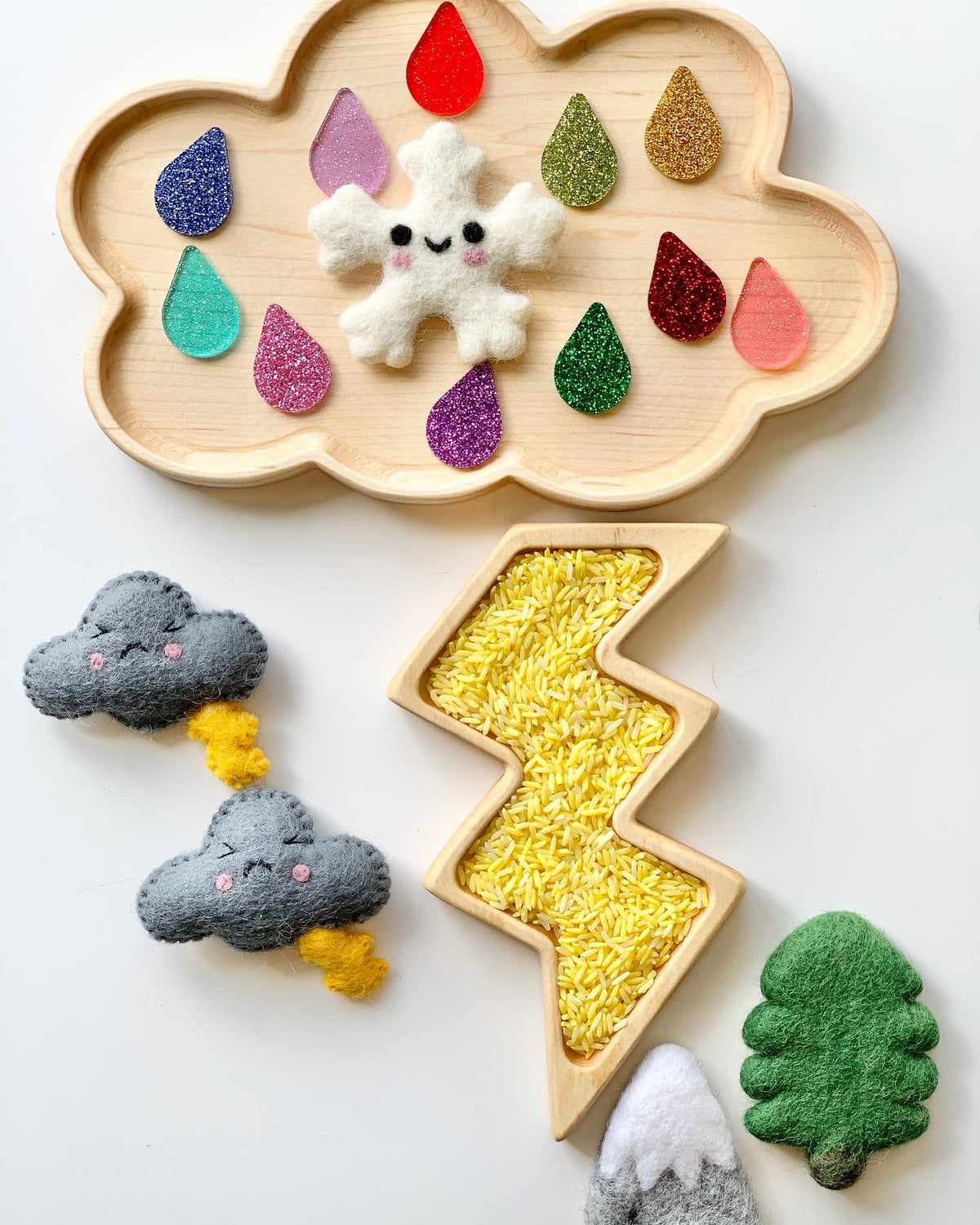 Wooden cloud-shaped sensory tray with colorful raindrop pieces, felt snowflake, lightning plate filled with yellow rice, and felt weather shapes