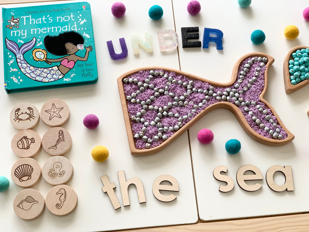 Wooden mermaid tail sensory tray filled with purple and silver beads with under the sea wooden letters and matching wooden sea creature tokens