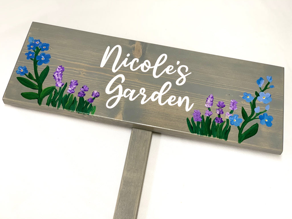 Large custom wooden garden sign painted gray with white cursive letters and hand-painted blue and purple flowers on wood grain background
