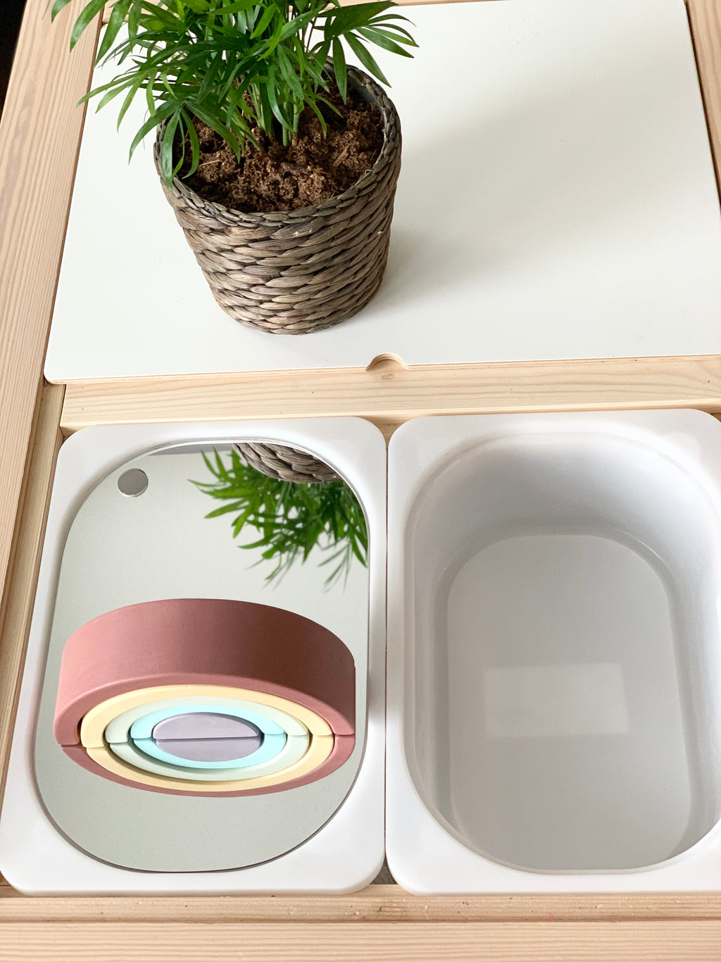 Mirrored acrylic Flisat table bin lid reflecting a plant and rainbow toy inside natural wood and white bin compartments