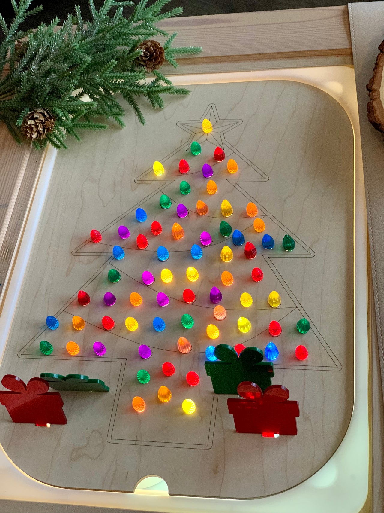 Wooden Christmas tree-shaped Flisat insert with colorful light-up pegs and acrylic present pegs on wooden table
