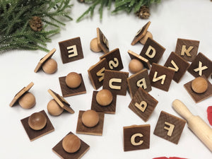 Wooden alphabet play dough stampers with engraved capital letters scattered on white surface with greenery background
