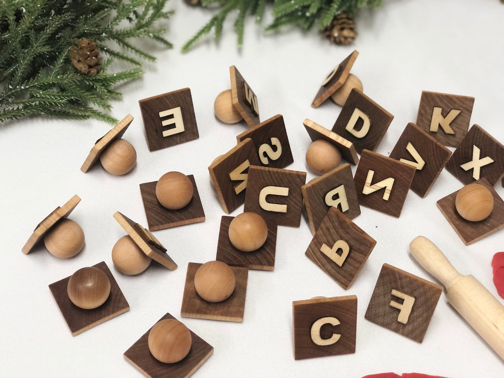 Wooden alphabet play dough stampers with engraved capital letters scattered on white surface with greenery background