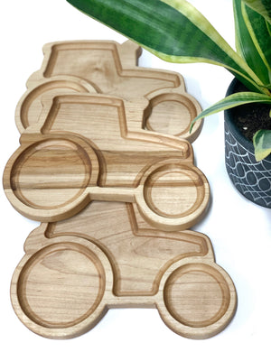 Three natural wooden tractor-shaped sensory trays stacked near green potted plant on white surface