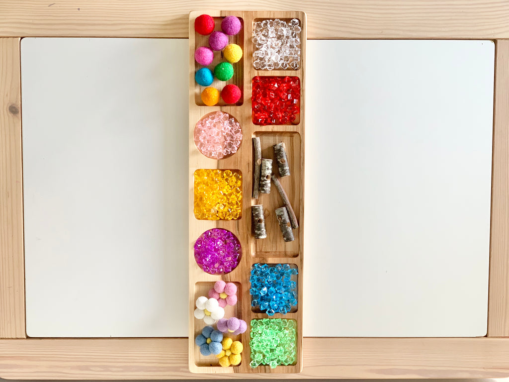 Extra large wooden tinker tray with colorful craft pom poms, beads, and small natural wood pieces on light wood table
