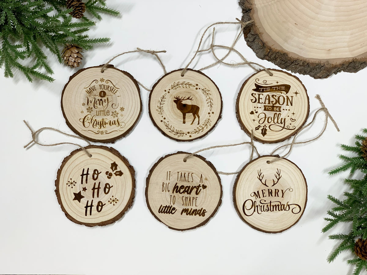 Set of six round wood burned Christmas ornaments with festive phrases and a reindeer illustration on natural wood slices