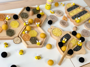 Set of natural wooden nesting hexagon plates with honeycomb shapes, bees, and yellow and black felt balls on white surface