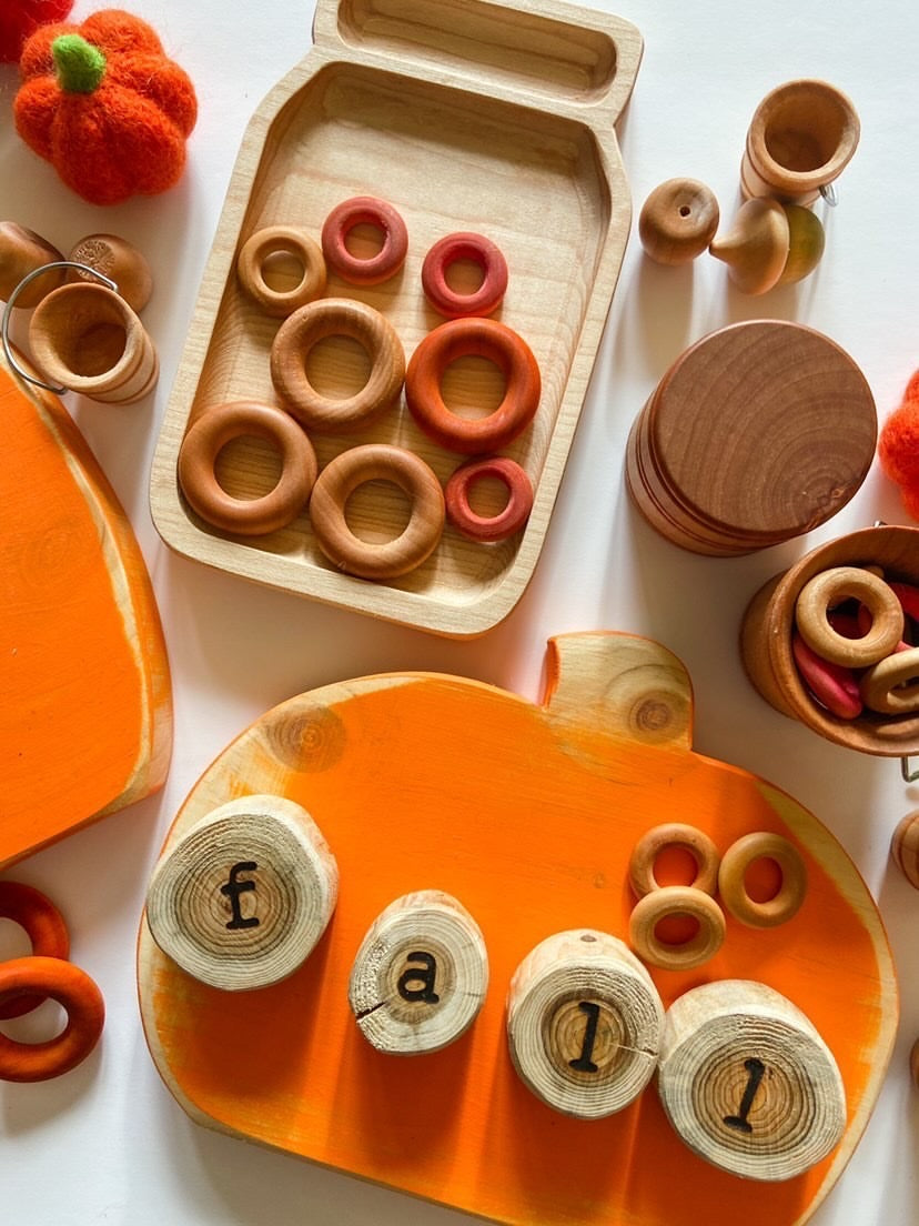 Small wooden sensory tray shaped like a jar with natural and stained wooden rings on white background
