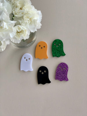 Set of five Halloween ghost laser cut acrylic shapes in white, orange, black, green glitter, and purple glitter on neutral surface