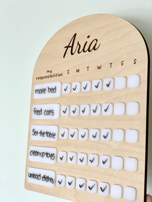 Personalized wooden chore chart with white acrylic dry erase pieces and weekly task checkmarks on light background
