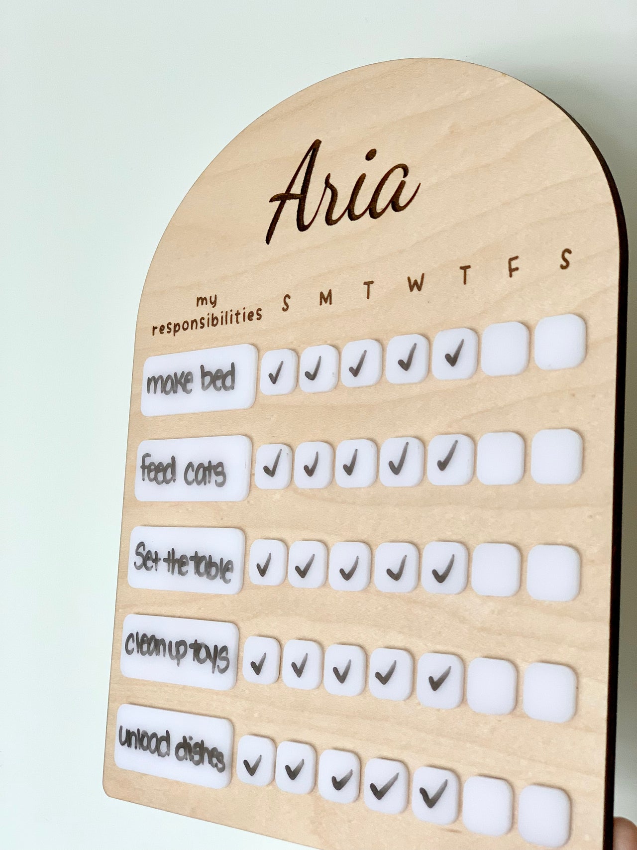 Personalized wooden chore chart with white acrylic dry erase pieces and weekly task checkmarks on light background