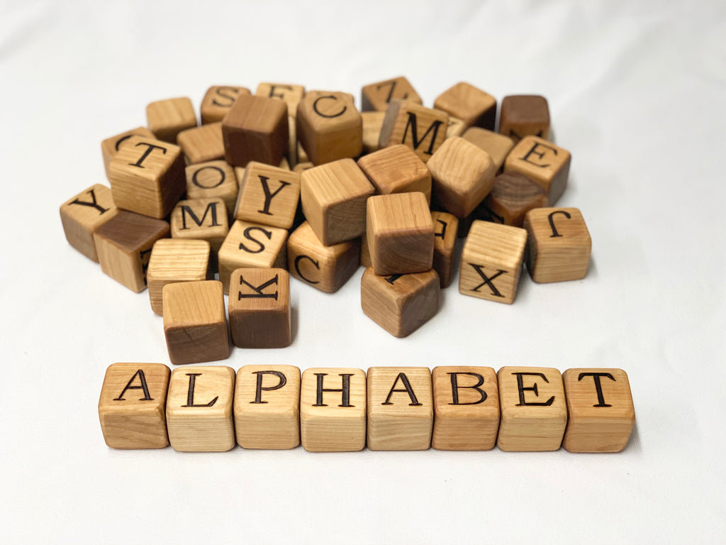 Natural wooden 2-inch alphabet blocks with engraved letters scattered and arranged to spell ALPHABET on white background