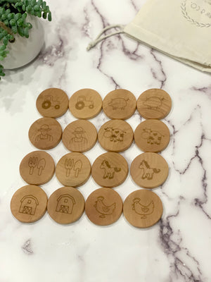 Wooden memory game pieces with engraved farm icons including tractor, pig, farmer, cow, tools, horse, barn, and chicken on marble surface