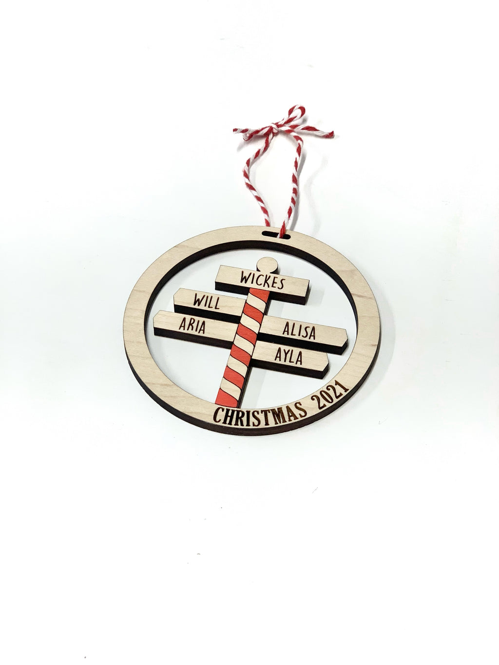 Round wooden Christmas ornament with personalized family names on striped North Pole sign and red white string hanger