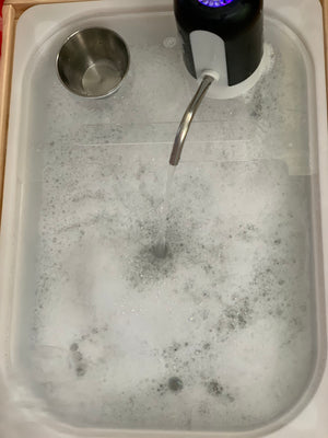 White play kitchen sink insert filled with soapy water and running water from black faucet accessory