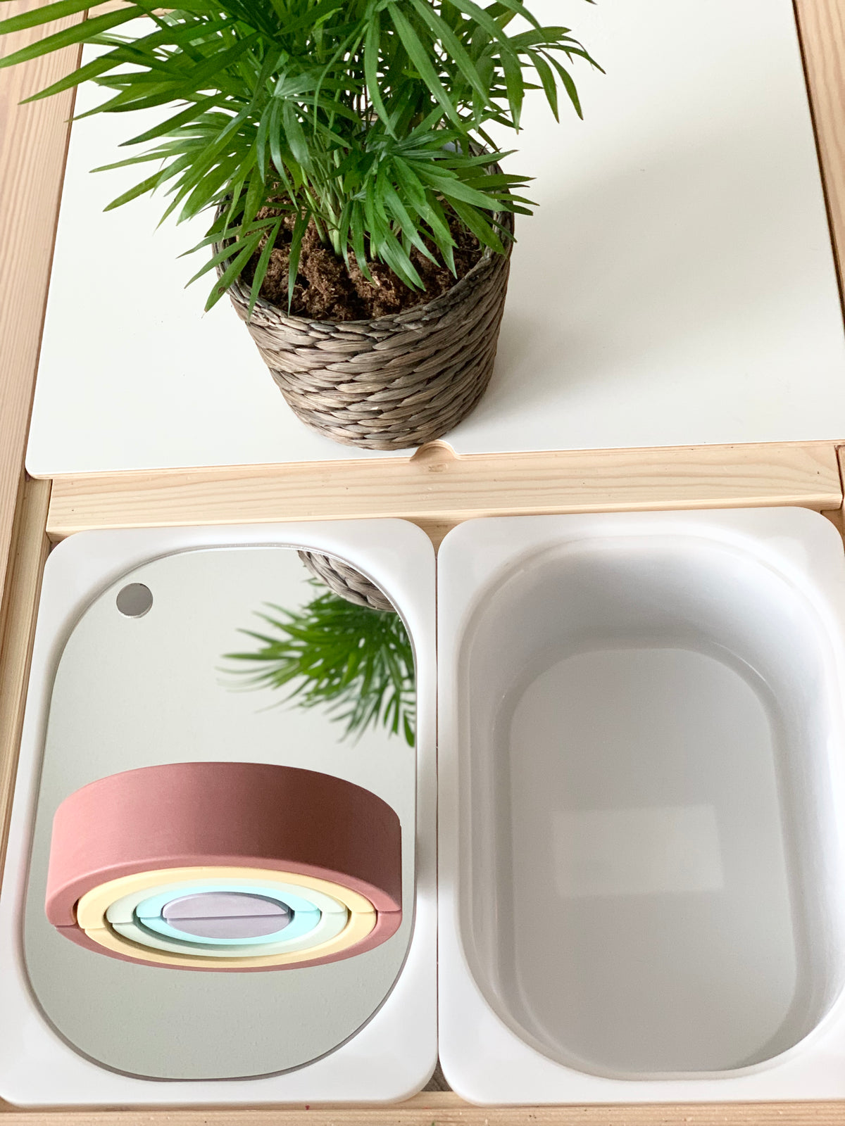 Small Flisat bin with premium mirrored acrylic table insert reflecting plant and wooden rainbow toy on white wood surface