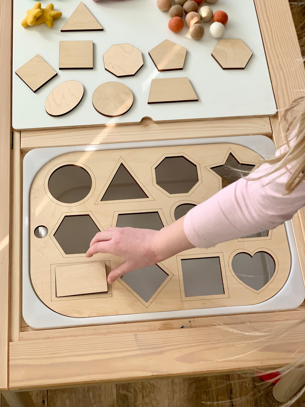 Child placing wooden rectangle piece into shape sorter Flisat table top insert with various geometric shapes on wooden table