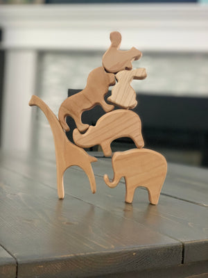 Natural wooden safari animal toy figurines stacked in balancing tower on wooden table surface