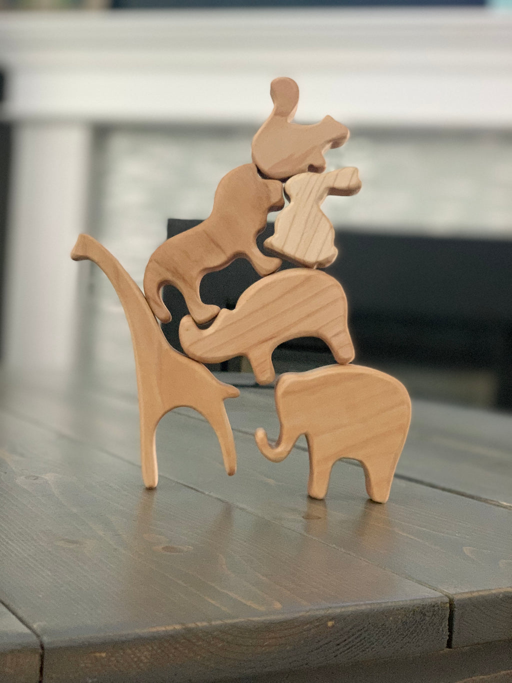 Natural wooden safari animal toy figurines stacked in balancing tower on wooden table surface