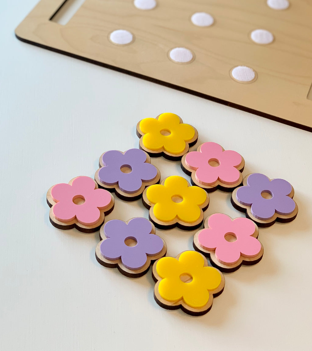 Wooden flower-shaped cookie pieces in pink, purple, and yellow with a cookie sheet in the background on white surface