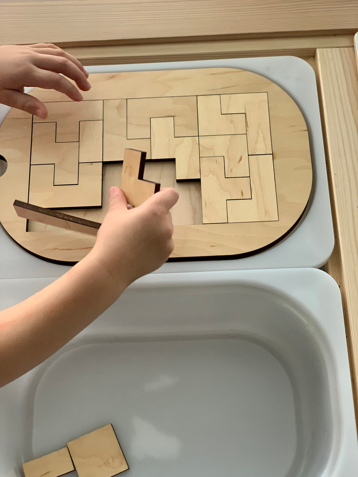 Small wooden puzzle Flisat table top insert fitted into storage bin with child’s hands holding pieces