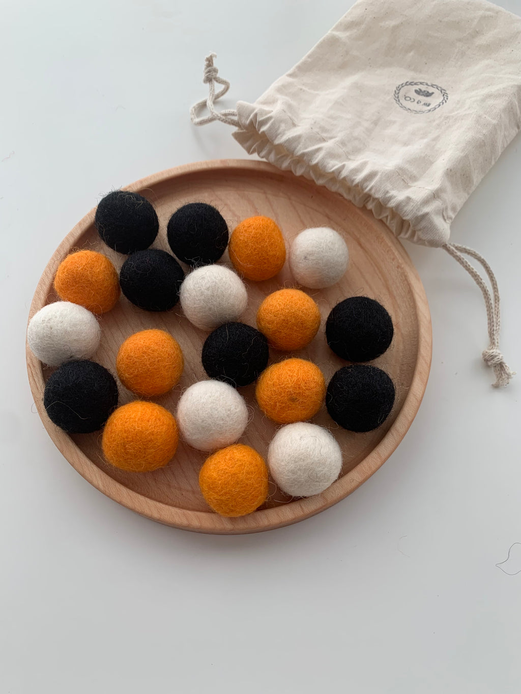 Assorted Halloween felt balls in black, orange, and white on round wooden plate with cloth drawstring bag