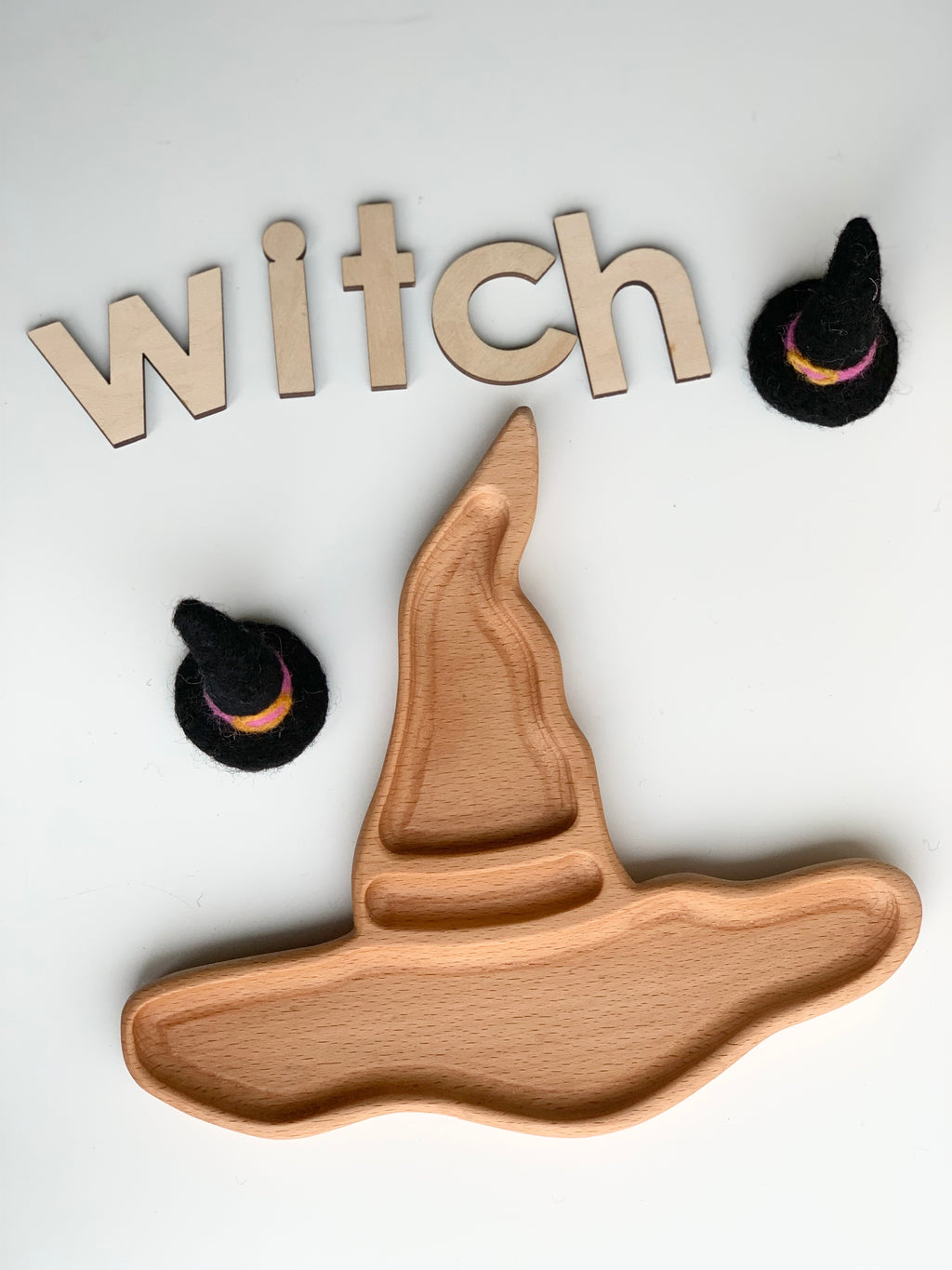 Natural wooden witch hat sensory tray with light wood letters spelling witch and two small black felt hats on white background